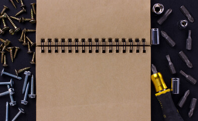 tools for repair and construction. Screwdriver with tips, furniture screws, measuring tape, self-tapping screws, notebook on a black background with a place for text. View from above