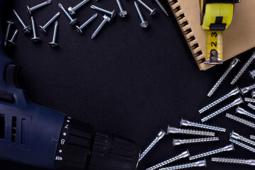 tools for repair and construction. Screwdriver, furniture screws, measuring tape, self-tapping screws, notebook on a black background with a place for text. View from above