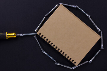 tools for repair and construction. Screwdriver, furniture screws, notebook on a black background with a place for text. View from above