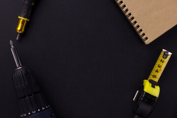 tools for repair and construction. Screwdriver, measuring tape, notepad on a black background with place for text. View from above