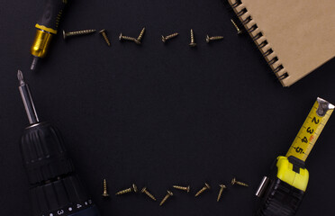 tools for repair and construction. Screwdriver, measuring tape, self-tapping screws, notebook on a black background with place for text. View from above