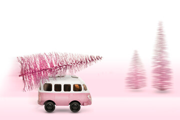 Christmas holiday concept with pine tree on toy car, pink Christmas tree on a retro minibus driven home from the forest. Copy space