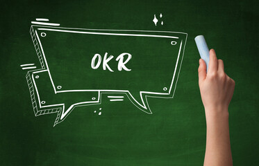 Hand drawing OKR abbreviation with white chalk on blackboard