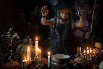Fototapeta na wymiar A cute little witch cooks a potion over a bonfire of herbs and mushrooms. Beautiful baby girl in witch costume with Halloween decoration