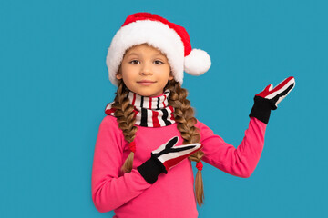 A little girl in a Christmas hat poses on a blue background for the new year.