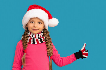 A little girl in a Christmas hat gives a thumbs up.