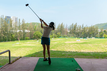 Asian golfer woman swing golf ball practice at golf driving range on evening on time for healthy sport. Lifestyle and Sport Concept. Healthy Sport.