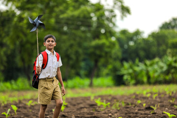 Cute indian child holding school bag and playing with pinwheel on road side