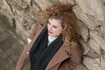 Portrait of a beautiful young woman near a stone wall. Outside. View from above