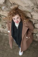 Portrait of a beautiful young woman near a stone wall. He looks up into the camera with a smile. Outside. View from above