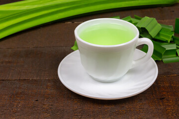 Pandan juice in white ceramic cup and fresh pandan leaves on wooden background.