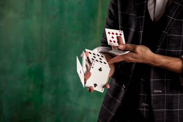 Close-up hands of young man with gambling cards. Handsome guy shows tricks with card. Clever hands of magician on green texture background. Concept of entertainment and Hobbies. Copy space