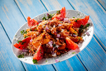 Penne with pork, tomato sauce, parmesan cheese, basil and vegetables served on wooden table
