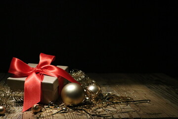 Banner of Christmas gift on a wooden table with a brown natural box and a red bow, gold and silver decorations with nuggets and golden tree branches. Black background.