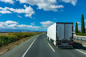Truck with refrigerated semi-trailer driving on a highway with a cloudy sky creating a beautiful landscape.