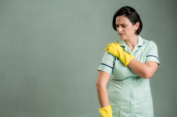 Young cleaning woman wearing a green shirt and yellow gloves has shoulder pain