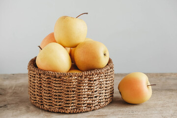 Yellow apples in a round wicker basket on a wooden table. Copy, empty space for text