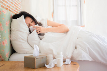 Sick asian woman sleeping in bed with high fever and medicine in foreground.