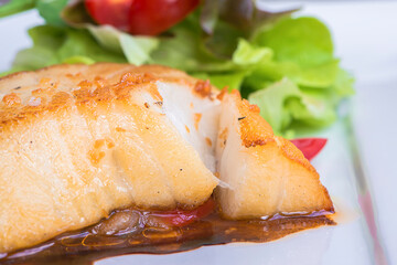 Close up fillet Snow fish grilled steak with sauce and Background blur fresh vegetable salad.