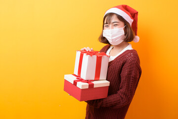 Portrait of young smiling woman in surgical mask wearing red Santa Claus hat isolated yellow background studio.