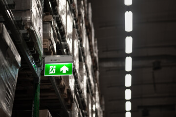 An electric lighting sign board of "Fire escape doorway" which is installed on the storage shelf in logistic warehouse.