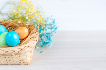 Multicolored Easter eggs lie in a basket that stands on a white wooden table.