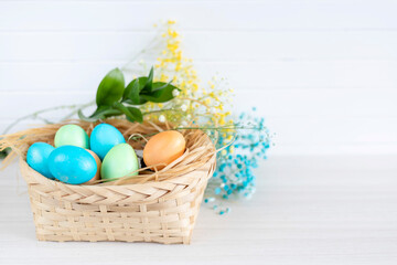 Multicolored Easter eggs lie in a basket that stands on a white wooden table.