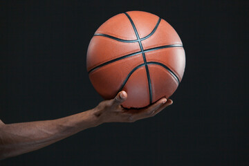 Photo of a black man hand holding a basketball isolated on black background.