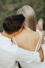 Close-up of backs of romantic couple in white clothes. Man delicately kissing a woman on her soft neck.