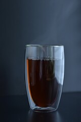 Double glass with black tea and steam on dark background