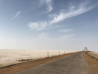 Beautiful empty path with  white sand on the sides and clear blue skies with few clouds.