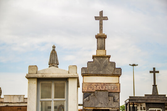 Topo de mausoléus, com uma imagem de santa e  cruzes em cemitério. Fotografia feita dentro do Cemitério Santana na cidade de Goiânia. 