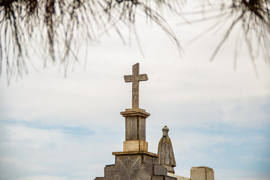 Topo de mausoléus, com uma imagem de santa e uma cruz em cemitério. Fotografia feita dentro do Cemitério Santana na cidade de Goiânia. 