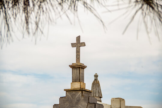 Topo de mausoléus, com uma imagem de santa e uma cruz em cemitério. Fotografia feita dentro do Cemitério Santana na cidade de Goiânia. 