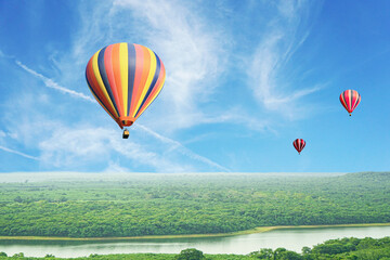 Colorful hot air balloons flying above high forest with beautiful sky background