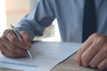 Close up of businessman with a pen in hand signing business contract on table in office