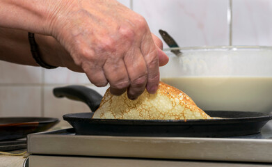 The woman's hands pour the pancake batter into a hot pan and fry them on both sides, turning them over with her hands.