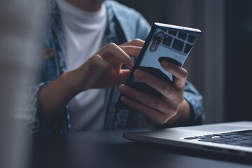 Woman hand using mobile phone during online working on laptop computer at night at home office