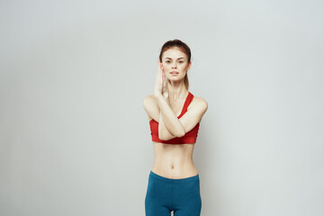 Fototapeta na wymiar A woman in a red T-shirt on a light background is engaged in fitness gestures with her hands a slim figure 