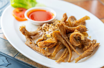 Deep-fried small fishes or Sillago fish with garlics. Crispy fried Sillago in white plate on table in resturant. Close up Thailand food image. Sillago or Pla Hed Cone in Thai language.