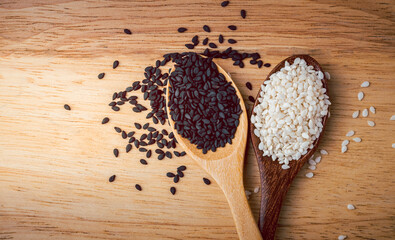 White and black sesame seeds in a wooden spoon in the background is a wooden table,organic  food concept.
