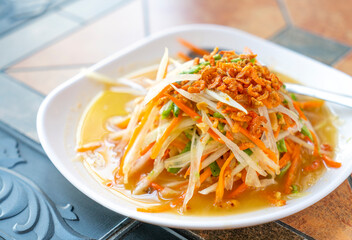 Som Tum or spicy papaya salad of traditional Thailand food, topping with dried small shrimps. Som Tum or spicy papaya salad in white plate on table in resturant, natural light. Close up food image.