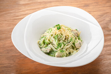 Tagliatelle pasta with pesto, chicken and Parmesan in a white plate on a wooden table