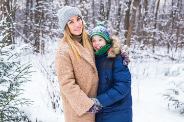 Portrait of happy mother with child son in winter outdoors. Snowy park. Single parent.