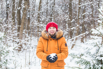 Fototapeta na wymiar Young man throwing snow in winter forest. Guy having fun outdoors. Winter activities.