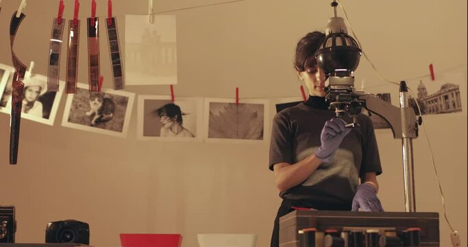Female photographer developing film and printing photographs in traditional process in darkroom. Portrait of creative girl photographer in photo studio darkroom. Developing analog camera film.