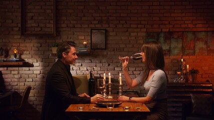Elegant couple having romantic dinner at home, sitting at table in living room drinking red wine. Stay at home concept.