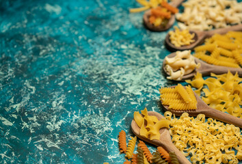 Various mix of dry pasta on wooden spoons.