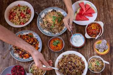 table full of healthy and colorful  food with detail of hands touching asian and Mediterranean food