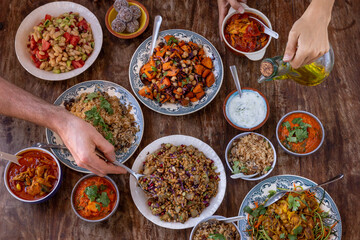 table full of healthy and colorful  food with detail of hands touching asian and Mediterranean food